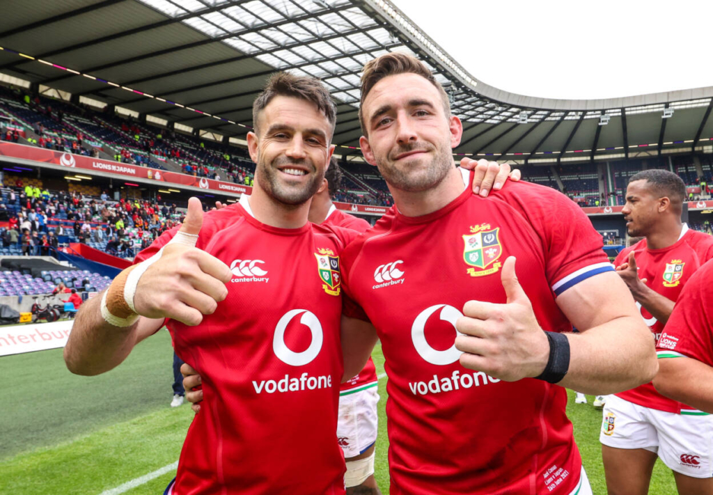 two men in sports uniforms giving thumbs up. Lions tour