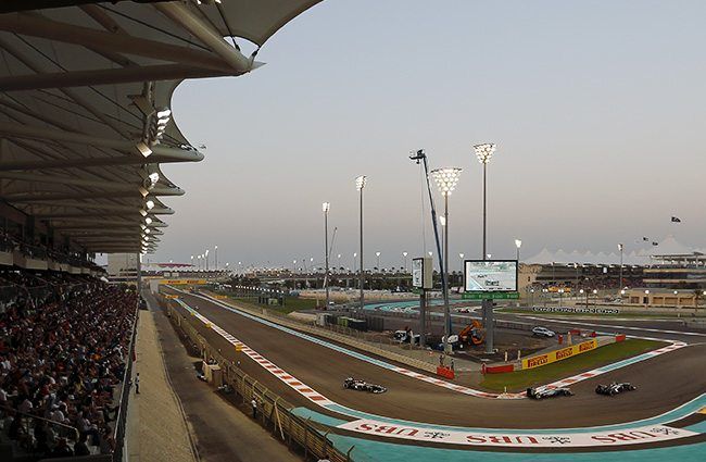Cars at speed below a packed grandstand at Yas Marina Circuit at dusk