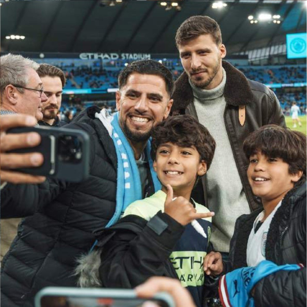 Guests taking a photograph with a Manchester City player pitchside