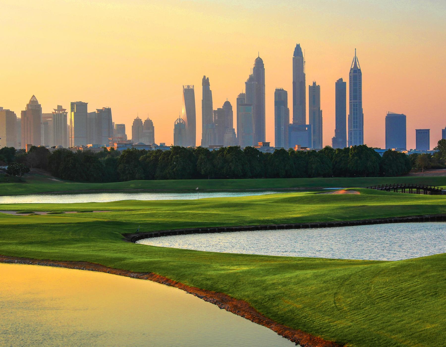 A Dubai golf course at sunset with the city skyline behind